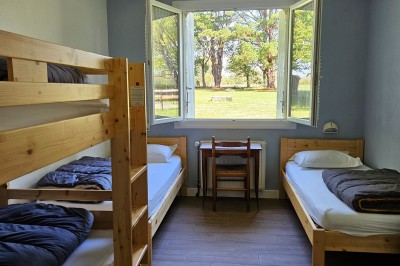Tente blanche montée sur une pelouse, équipée de tables hautes, devant un bâtiment clair et des arbres.