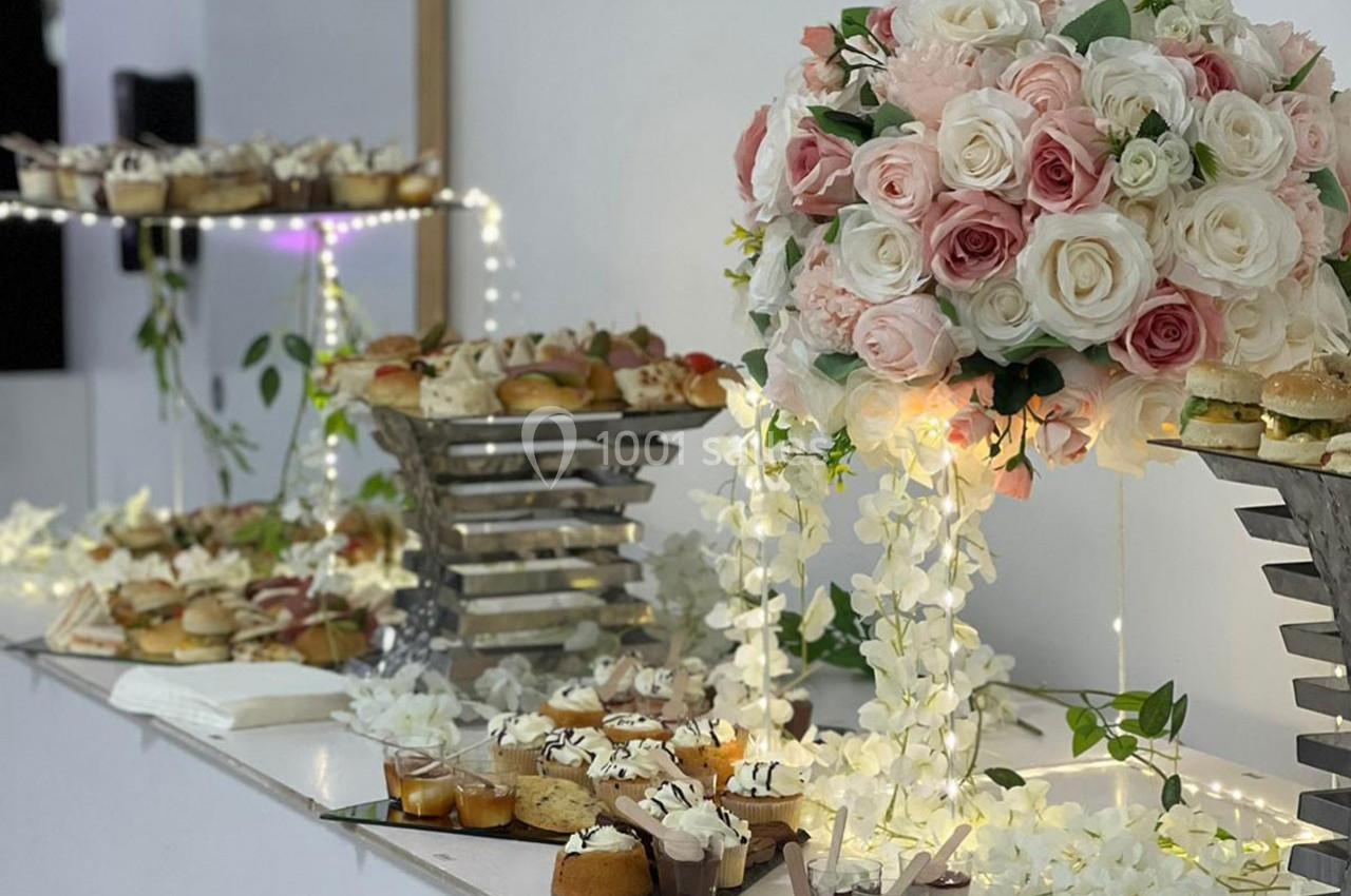 Buffet décoré avec des fleurs blanches et roses, présentant des pâtisseries et amuse-bouches sur des présentoirs élégants.