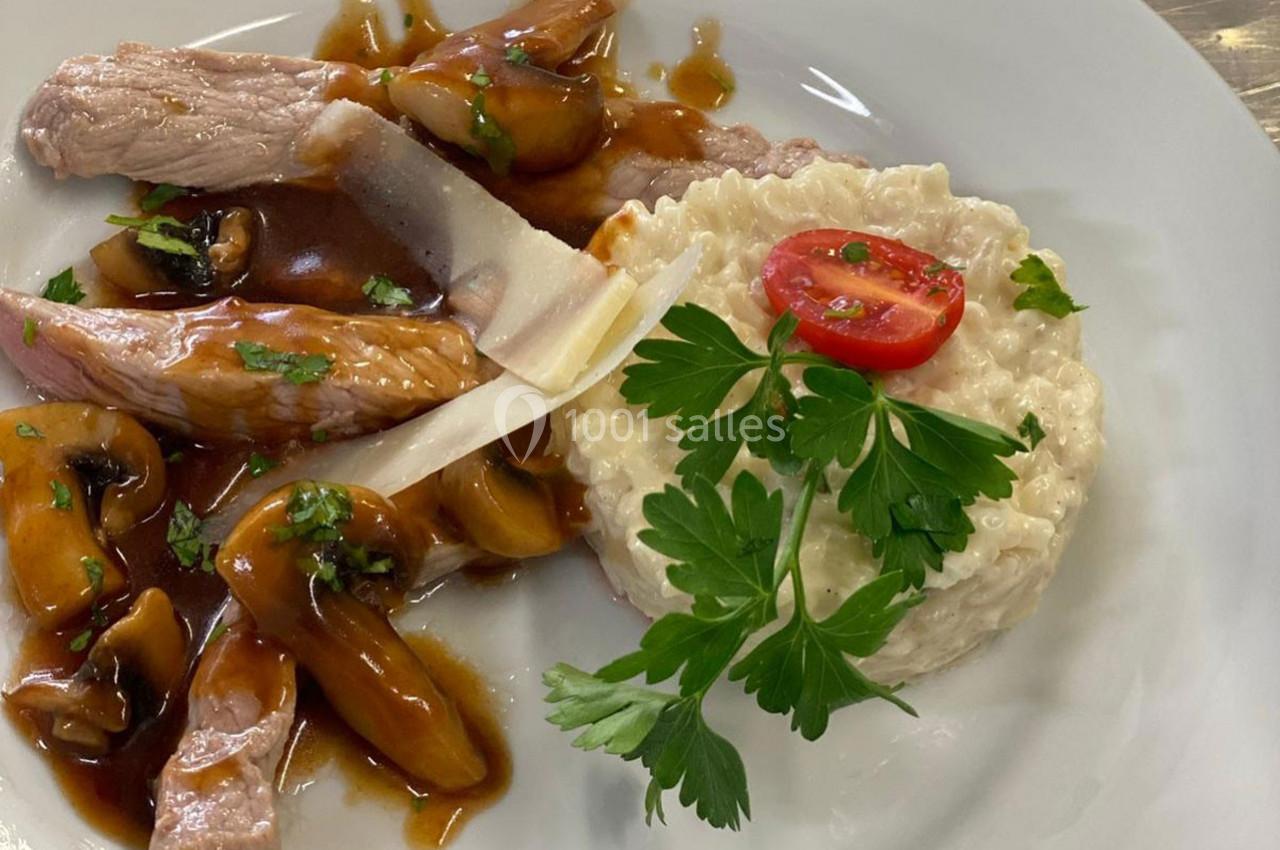 Assiette contenant du risotto crémeux, émincé de viande avec sauce aux champignons, tomate cerise et persil.