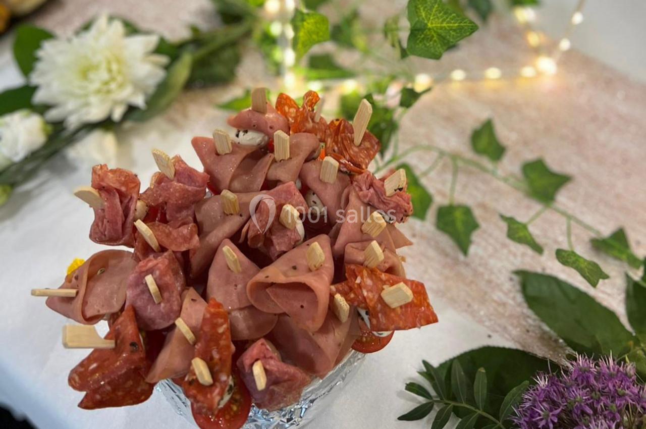 Brochettes apéritives composées de charcuterie, présentées sur un support, avec une décoration florale en arrière-plan.