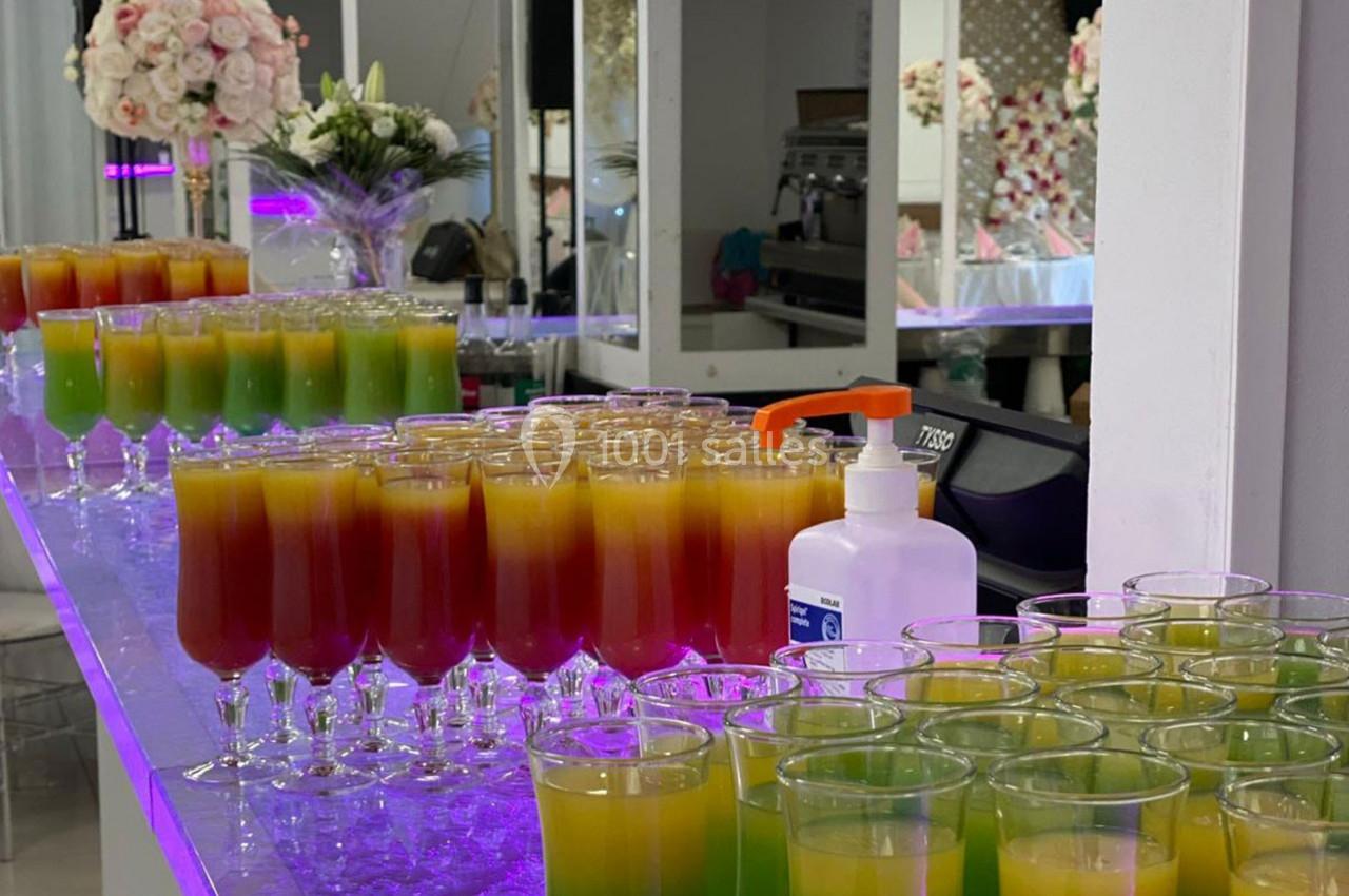 Verres de cocktails colorés alignés sur un comptoir lumineux, avec des décorations florales en arrière-plan.