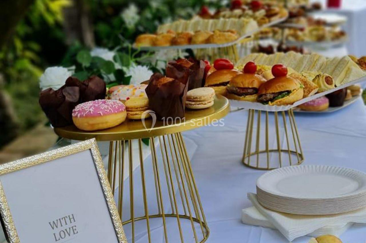 Buffet avec pâtisseries, sandwichs et desserts variés disposés sur des plateaux dorés sur une table blanche.