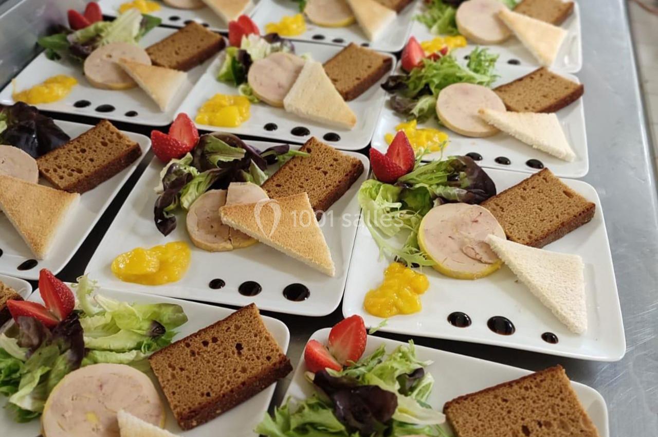 Assiettes dressées avec foie gras, pain, salade, fraises et sauce, disposées sur une table en inox.