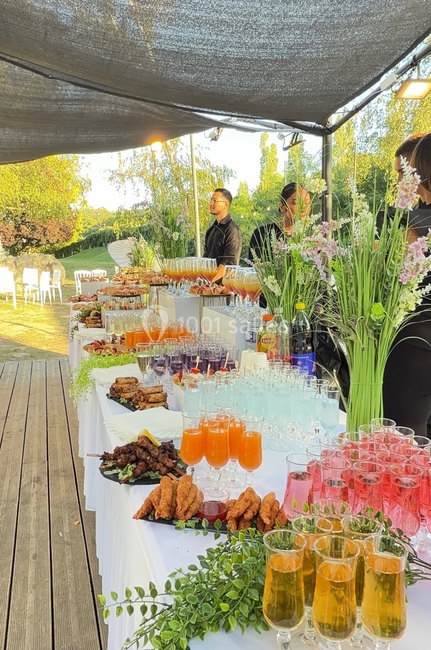 Buffet extérieur avec boissons colorées, plats variés et décoration florale, sous une tonnelle ensoleillée.