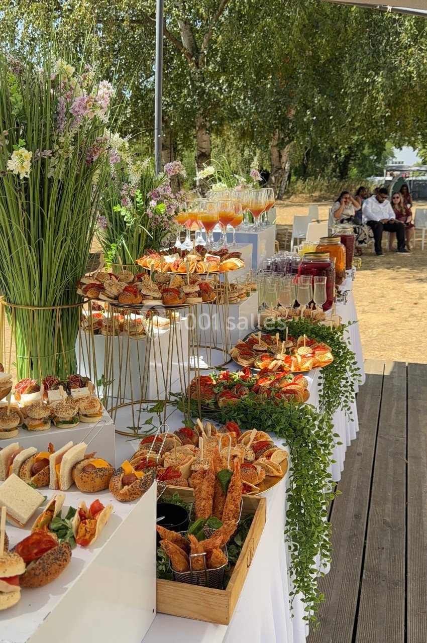 Buffet en plein air avec une variété de plats, boissons et décorations florales, installé sous une tente.