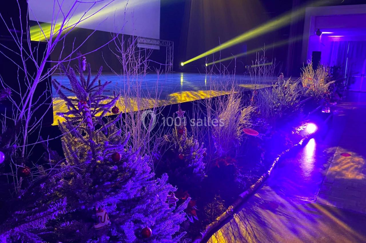 Scène illuminée avec projecteurs jaunes et décorations végétales hivernales, incluant sapins et branchages.