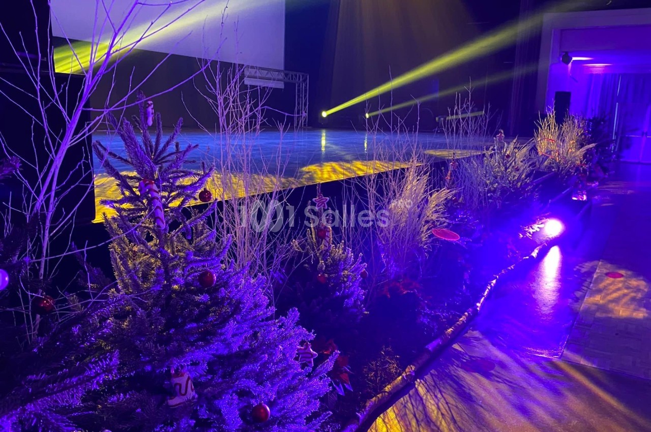 Scène illuminée avec projecteurs jaunes et décorations végétales hivernales, incluant sapins et branchages.