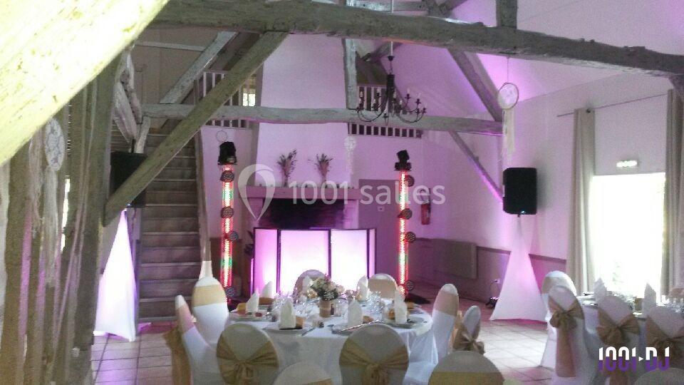 Salle de réception décorée avec des tables dressées, des chaises ornées de nœuds et un éclairage coloré près d'une cheminée.