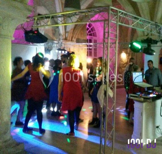 Groupe de personnes dansant sous des jeux de lumière colorés dans une salle avec des arches en pierre.