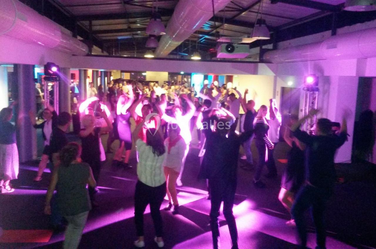 Groupe de personnes dansant sous des lumières colorées dans une salle avec un plafond industriel.