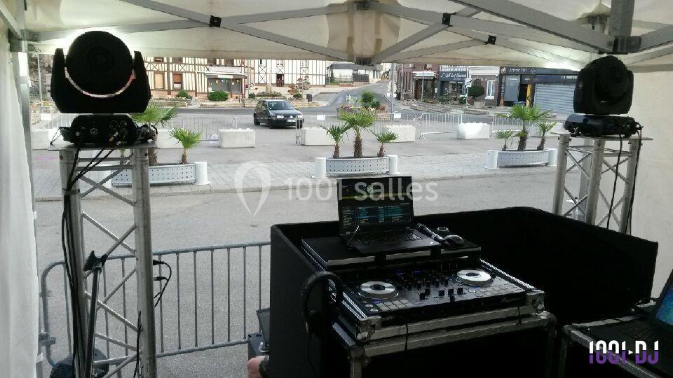 Équipement de DJ installé sous un chapiteau, avec platines, ordinateur et enceintes, donnant sur une place publique.