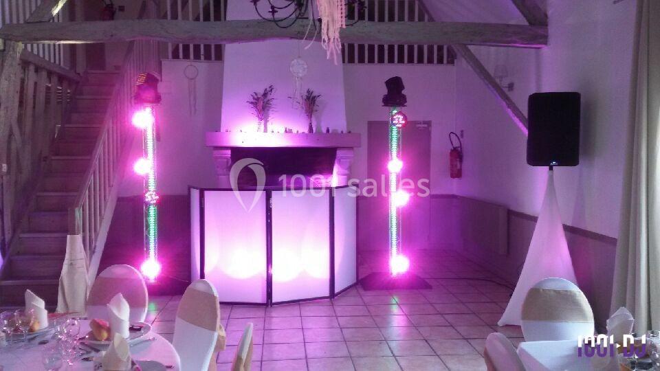 Salle de réception avec éclairage coloré, tables dressées et espace DJ équipé devant une cheminée.