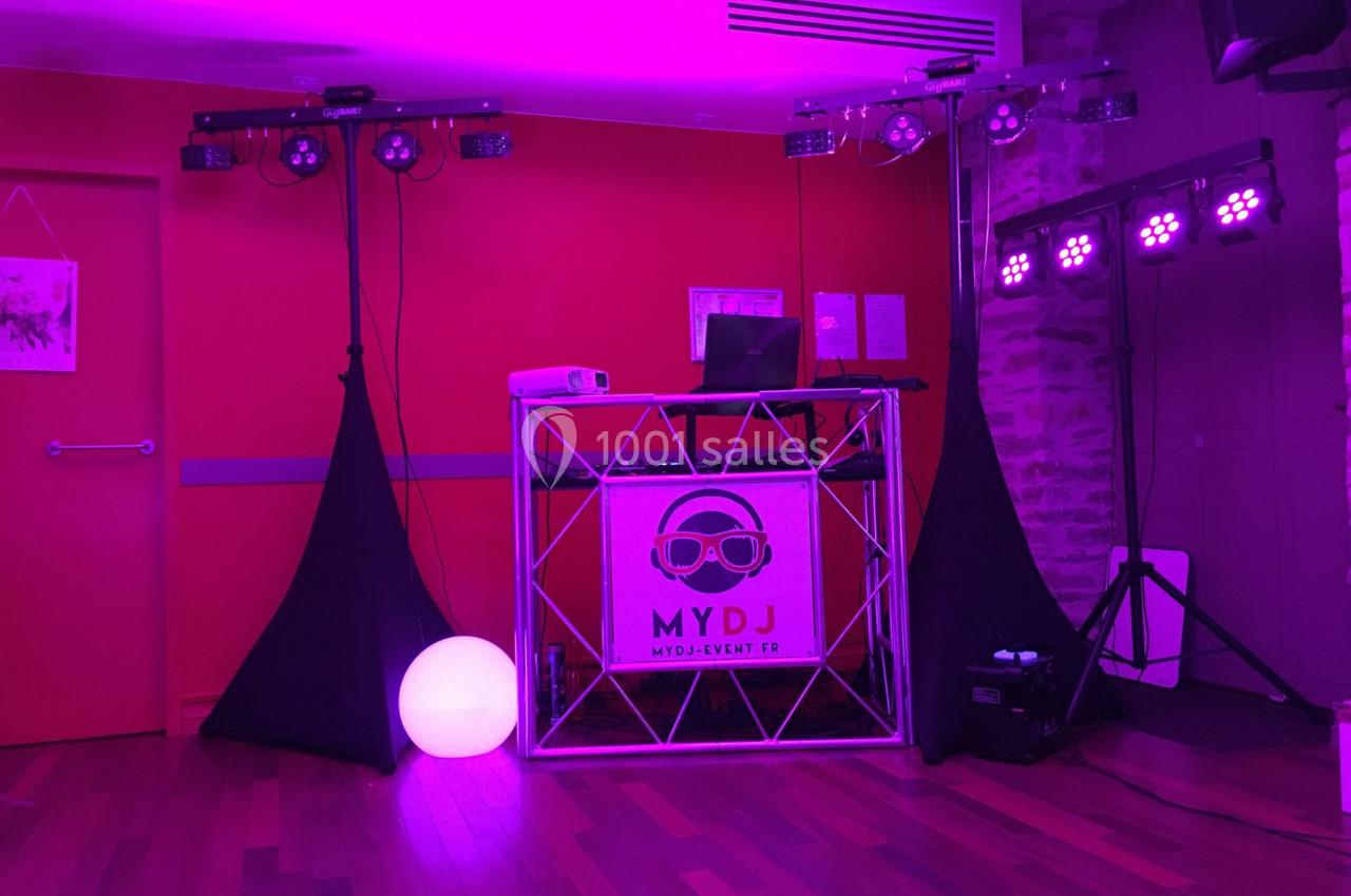 Stand de DJ avec éclairage violet, table de mixage, ordinateur portable et décorations lumineuses dans une salle.