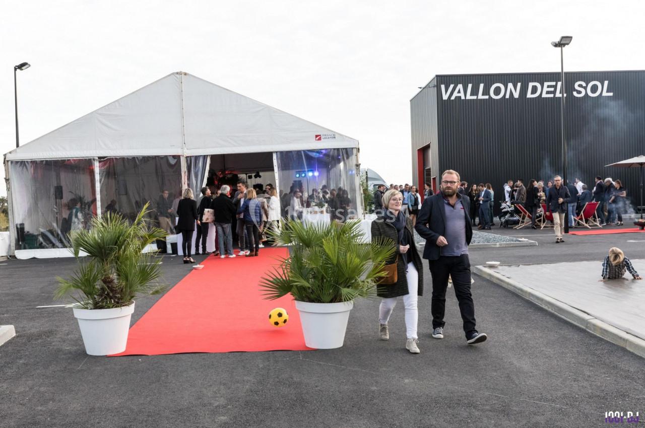 Entrée d'un événement sous chapiteau avec tapis rouge, plantes en pot et participants rassemblés à l'extérieur.