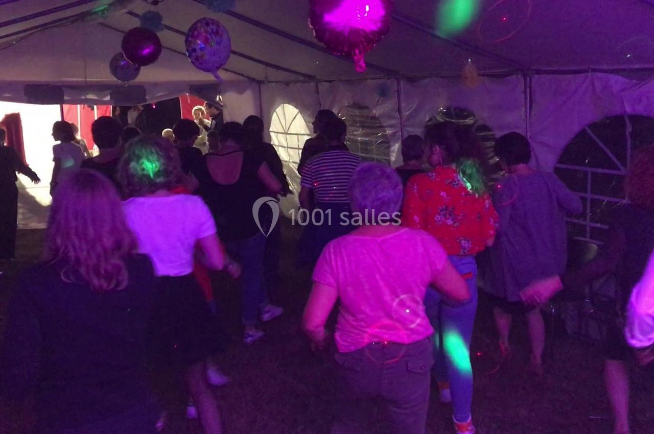 Des personnes dansent sous une tente éclairée par des lumières colorées lors d'une fête en soirée.