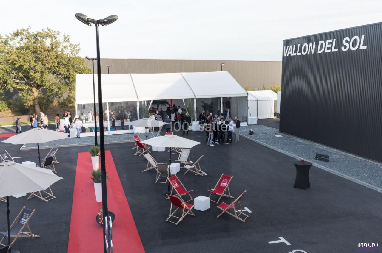 Vue d'un événement en extérieur avec des chaises longues, parasols, tapis rouge et une tente blanche accueillant des…
