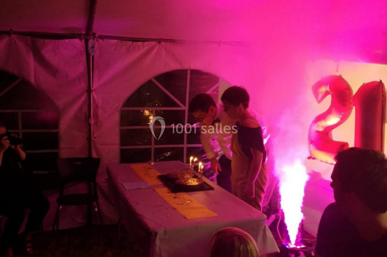 Deux personnes soufflent des bougies sur un gâteau d'anniversaire dans une tente éclairée par des lumières roses.