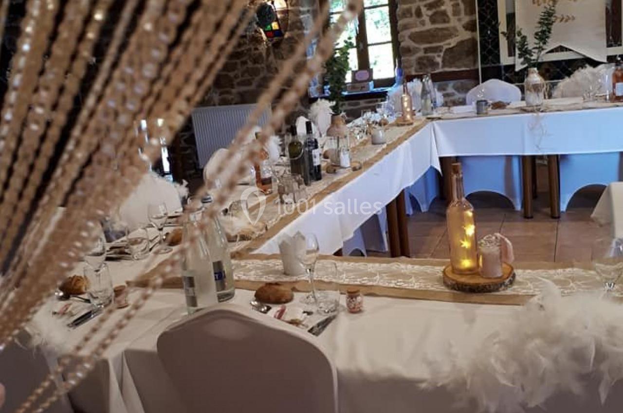Salle décorée pour un événement, avec tables dressées, nappes blanches, bougies et guirlandes lumineuses.