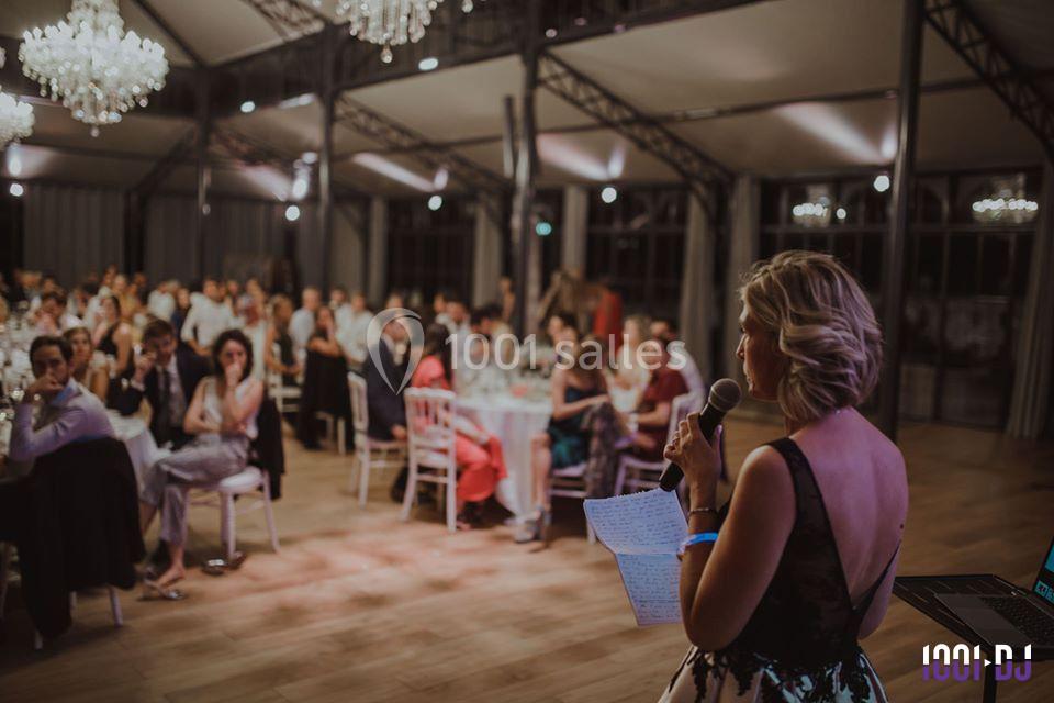 Une femme parle au micro devant un public assis dans une salle éclairée par des lustres.