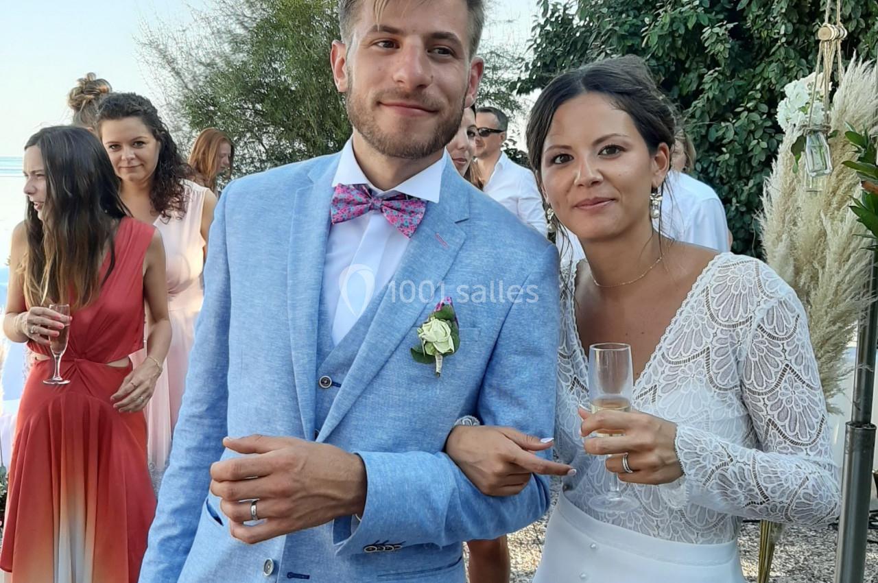 Un couple habillé élégamment, tenant des verres, pose en extérieur lors d'un événement festif.