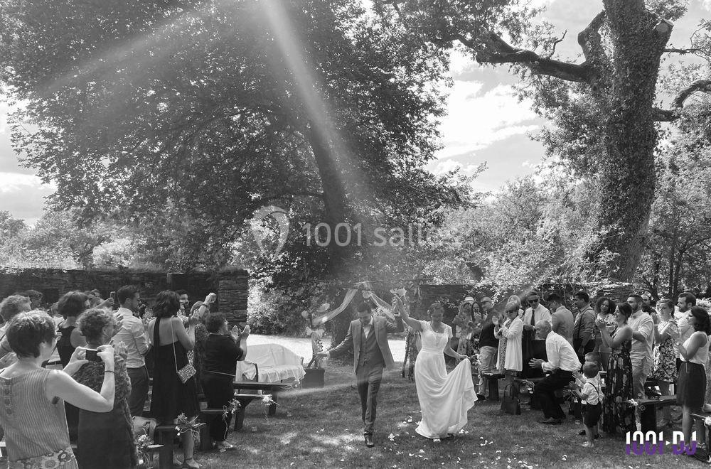 Un couple marche main dans la main sous les applaudissements des invités lors d'une cérémonie en plein air.