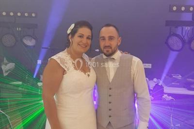 Un couple en tenue de mariage pose devant des lumières colorées dans une ambiance festive.