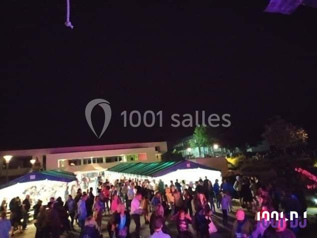Foule rassemblée de nuit devant des stands éclairés sous des tentes, dans un espace extérieur.