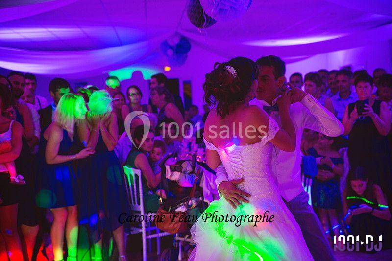 Un couple danse lors d'une fête, entouré d'invités sous des lumières colorées dans une salle décorée.