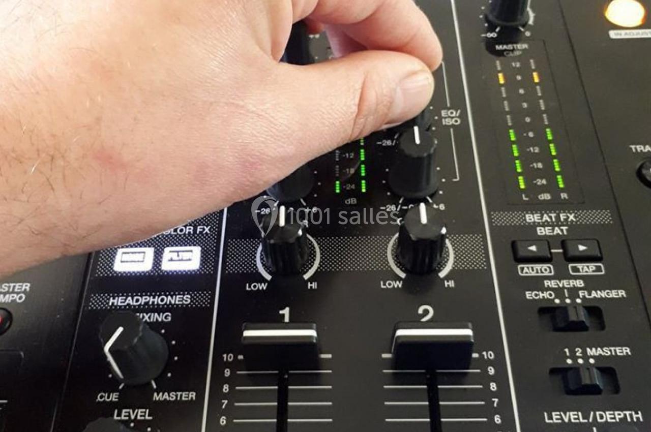 Main ajustant les réglages d'un mixeur audio DJ avec des boutons et curseurs visibles sur la console.