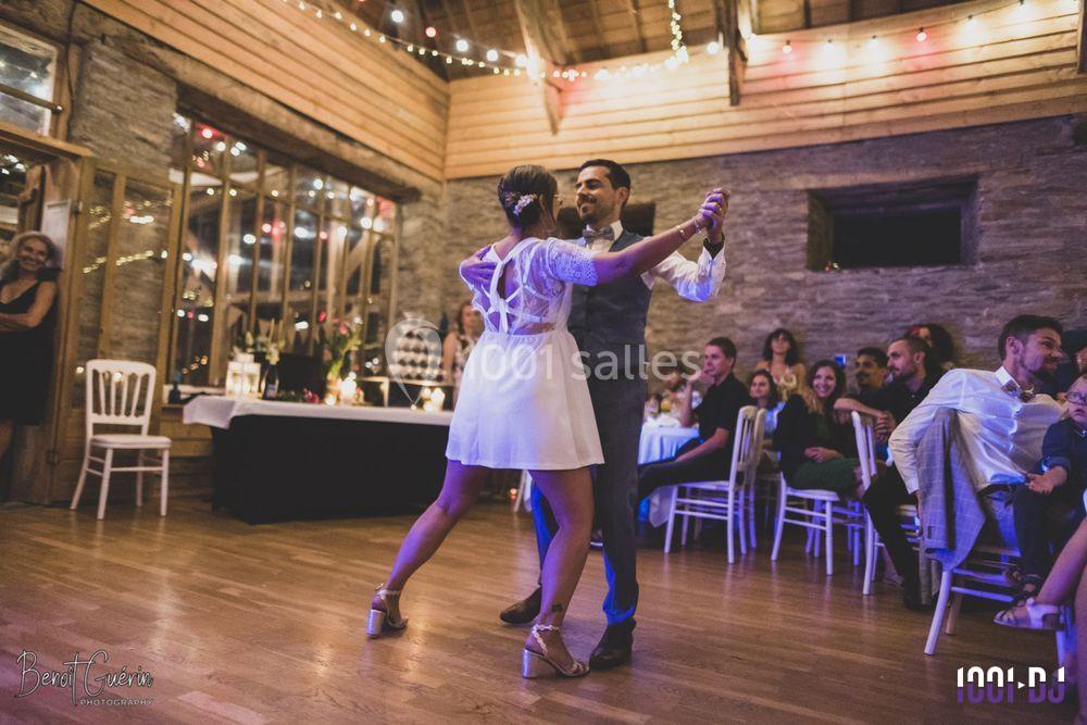 Un couple danse dans une salle en bois décorée de guirlandes lumineuses, devant des invités assis.