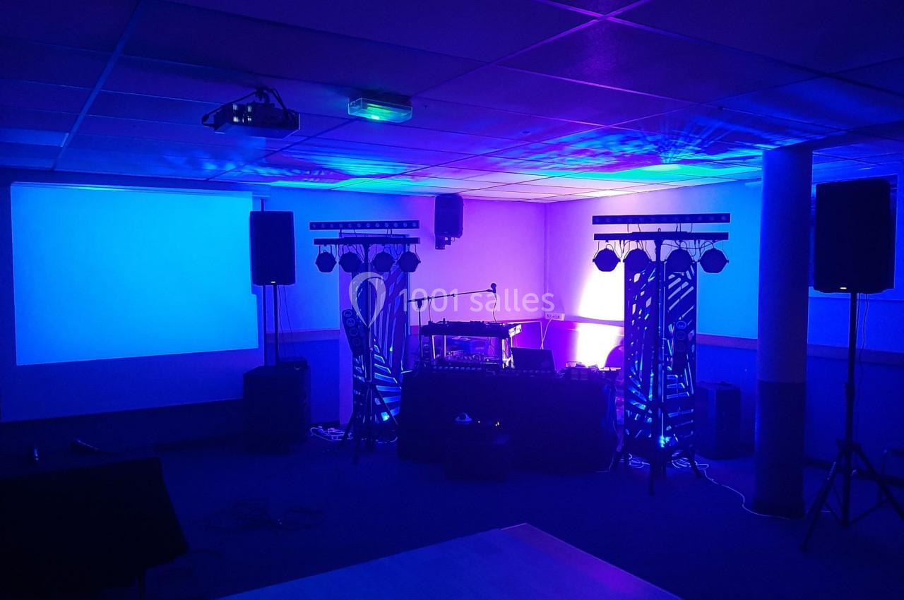 Salle équipée pour un événement avec éclairage coloré, projecteurs, enceintes et matériel audio sur scène.
