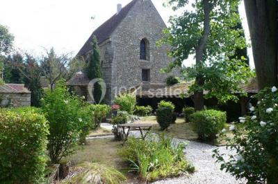 Ruelle pavée bordée de fleurs, avec un puits en pierre et des bâtiments anciens sous un ciel ensoleillé.
