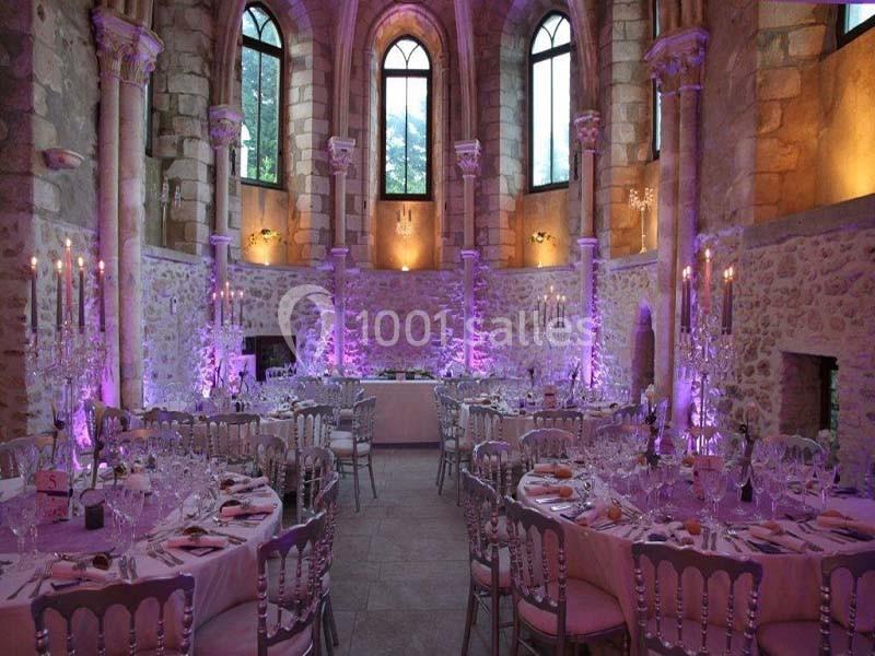 Salle de réception dans une ancienne chapelle en pierre, décorée de lumières violettes et de tables élégantes.