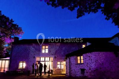 Ruelle pavée bordée de fleurs, avec un puits en pierre et des bâtiments anciens sous un ciel ensoleillé.