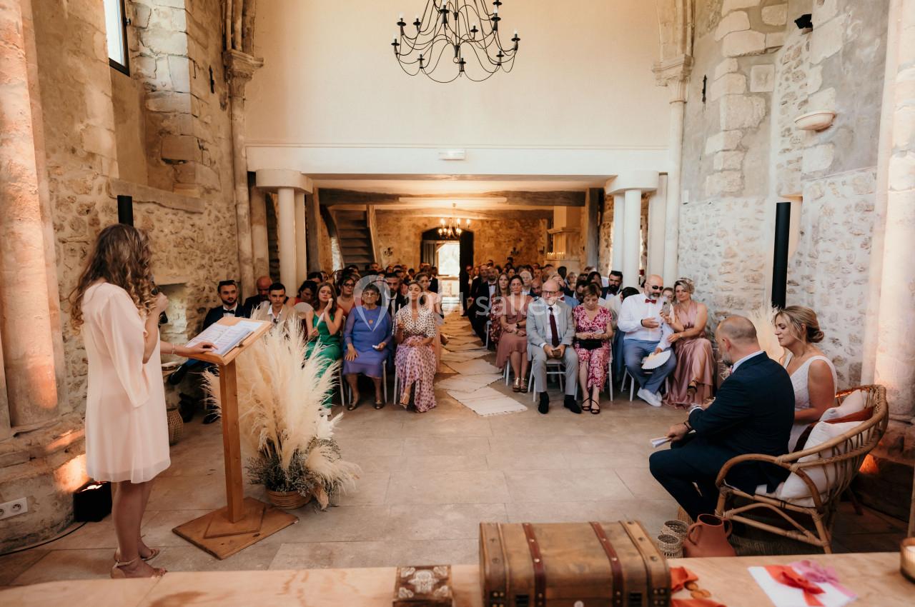 Une cérémonie dans une salle en pierre, une femme parle à un pupitre devant un public assis.