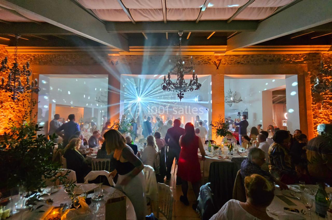 Salle de réception animée avec des invités assis et debout, éclairage coloré et jeux de lumière sur la piste de danse.