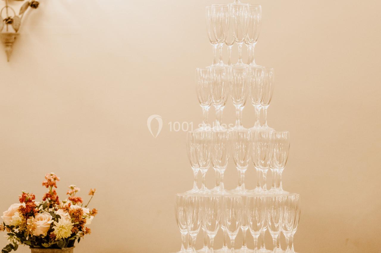 Tour de coupes en verre empilées pour un service de champagne, décorée de fleurs sur une table blanche.
