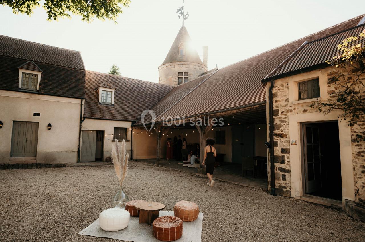 Cour intérieure d'un bâtiment ancien avec une tour, des décorations et des invités sous un auvent éclairé.