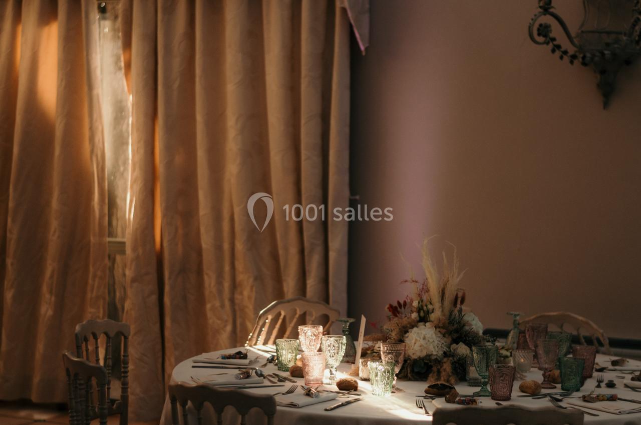 Table ronde élégamment dressée avec des verres colorés et un centre de table floral, éclairée par une lumière tamisée.