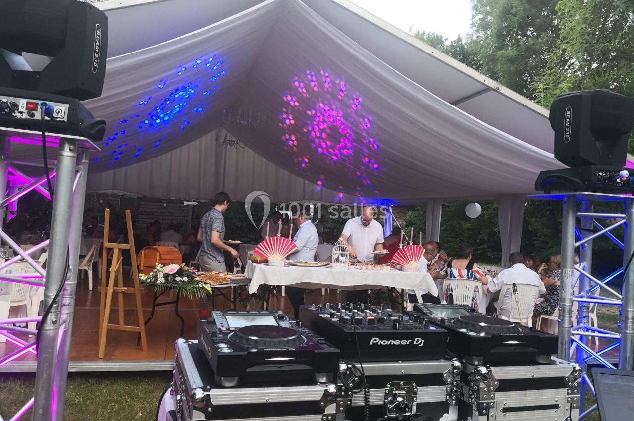 Tente blanche décorée avec éclairages colorés, tables dressées pour un buffet et matériel de DJ au premier plan.