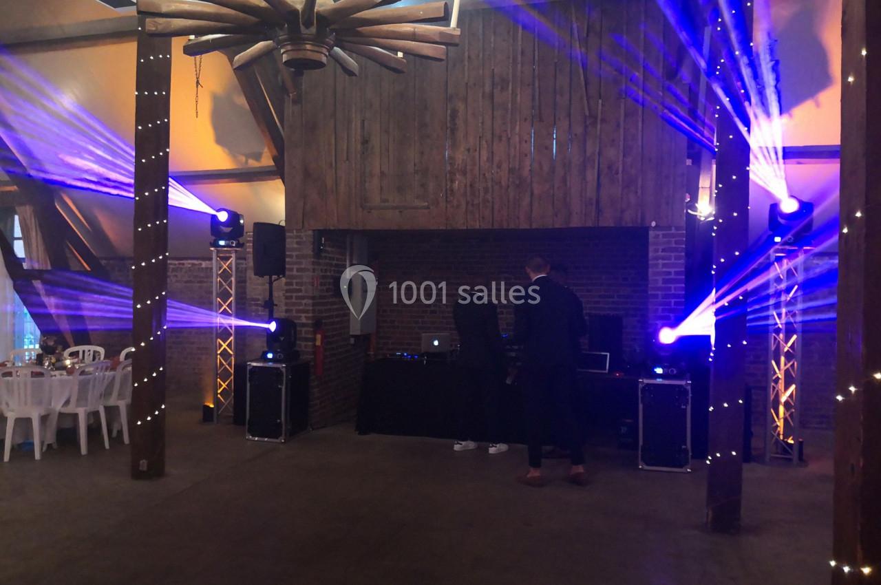 Deux personnes ajustent un équipement de DJ dans une salle décorée avec des lumières colorées et des poutres en bois.