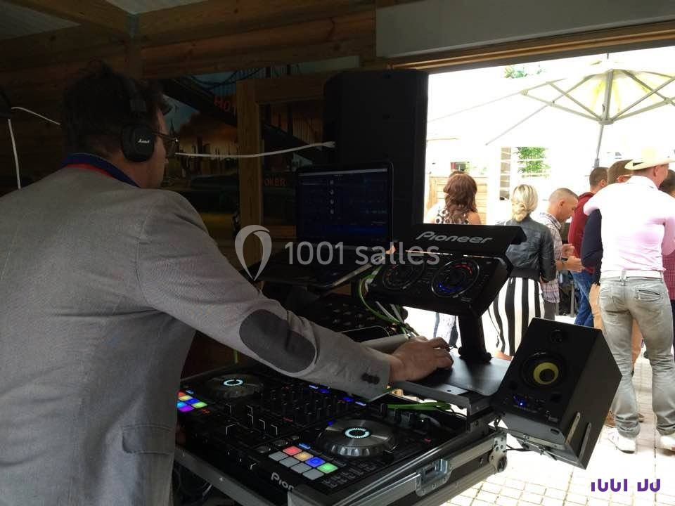 Un DJ mixe de la musique sur une console dans un espace ouvert, avec des personnes discutant en arrière-plan.