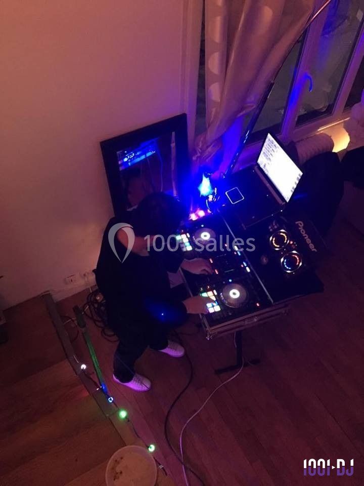 Un DJ mixant sur une console avec des lumières colorées dans une pièce au sol en bois.