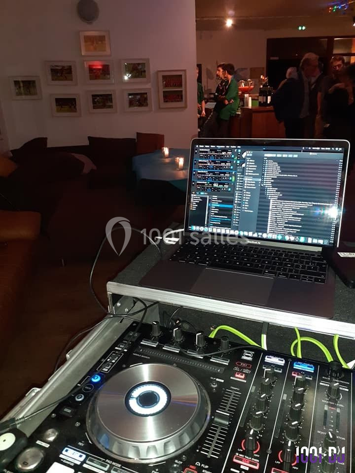 Un poste de DJ avec une table de mixage et un ordinateur portable dans un espace intérieur avec des personnes en arrière…