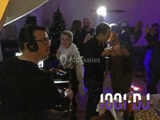 Vue d'une soirée avec un DJ en arrière-plan, des invités dans une ambiance tamisée et un écran de mixage au premier plan.