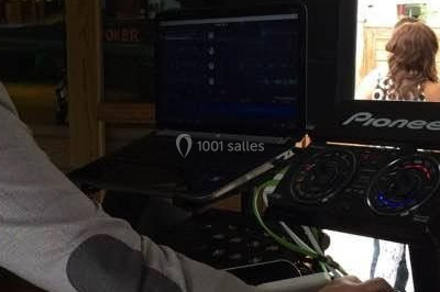 Vue d'une soirée avec un DJ en arrière-plan, des invités dans une ambiance tamisée et un écran de mixage au premier plan.