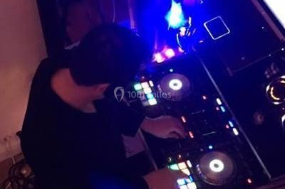 Vue d'une soirée avec un DJ en arrière-plan, des invités dans une ambiance tamisée et un écran de mixage au premier plan.