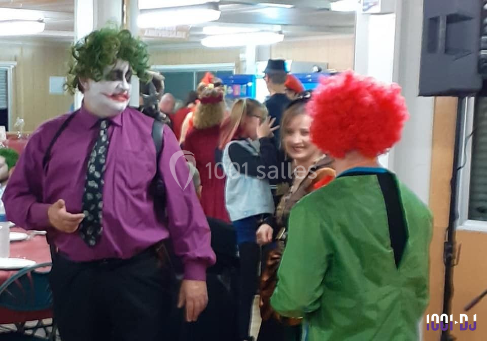 Des personnes déguisées, dont un homme maquillé en clown, discutent dans une salle animée lors d'un événement festif.