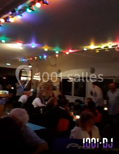 Salle animée avec des convives assis, éclairée par des guirlandes lumineuses colorées au plafond.