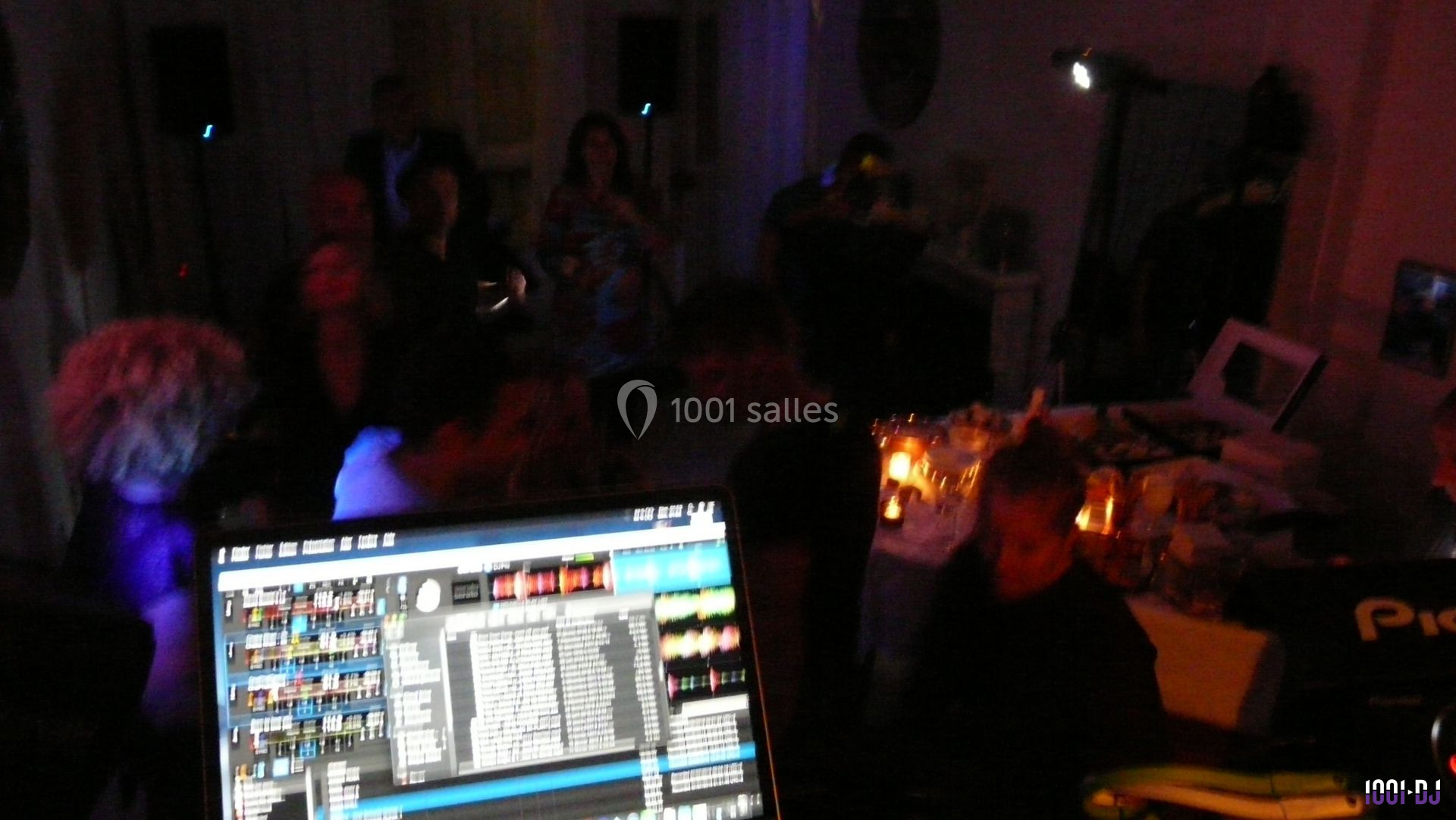 Vue d'une soirée avec un DJ en arrière-plan, des invités dans une ambiance tamisée et un écran de mixage au premier plan.